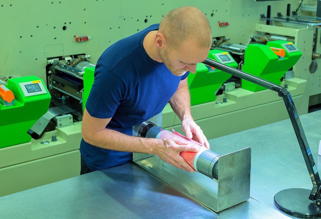 Technician inspecting and preparing a flexographic printing plate cylinder, ensuring accurate setup for multi-colour packaging production.